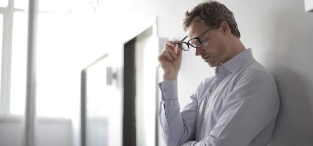 Man with glasses leaning against a wall